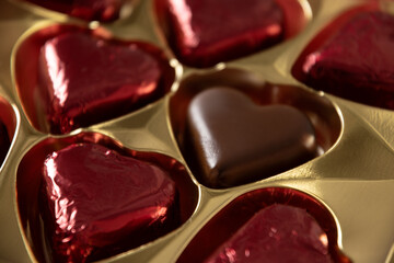 Heart shaped romantic chocolate candy sweets in red foil in box. Valentine's day card. Close up.