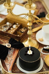 Black cake on a dark background with golden jewelry. A cake for Birthday A pie decorated with candle. Festive dessert with berries.
