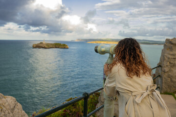 Tourist using binoculars looking at mouro island from magdalena peninsula in santander, spain