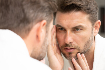 a well-groomed adult man looks in the mirror for well-groomed, wrinkle-free skin. Handsome man...