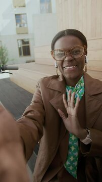 Vertical UGC handheld shot of Black businesswoman in glasses and brown coat gesturing emotionally and talking about her projects, then ends shoot by tapping her finger on phone screen