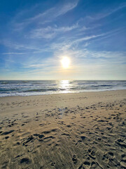 a beautiful sunrise at the beach with footprints in the sand, ocean water and waves, blue sky and clouds in Carolina Beach North Carolina USA