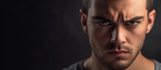 Obraz premium Intense young man displaying seriousness with furrowed brows and ample space for text overlay on a dark background