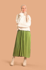 Beautiful young happy Muslim woman in hijab on brown background