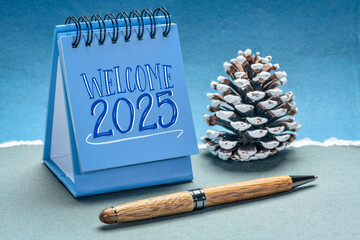 welcome 2025 in a spiral desktop calendar with a decorative frosty pine cone against handmade...
