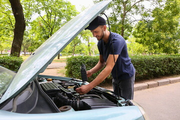Male mechanic refilling car oil outdoors