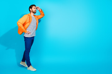 Fashionable young man in orange jacket and striped shirt gazing into the distance against a vibrant teal background