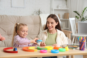 Nanny and cute little girl playing with toys on table at home