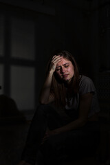 Sad woman sitting in dark room holding head
