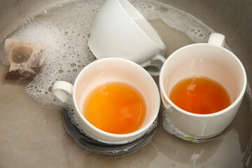 Metallic kitchen sink with cups of tea and soap water, closeup