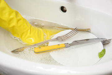 Female hand in rubber glove cleaning dishes in ceramic kitchen sink, closeup