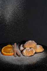 orange cookies and cinnamon powdered sugar on black background kitchen concept