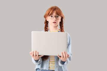 Naklejka premium Shocked teenage redhead girl with laptop on light background