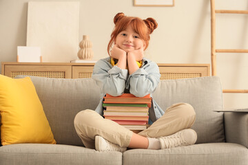 Teenage redhead girl with books sitting on sofa at home