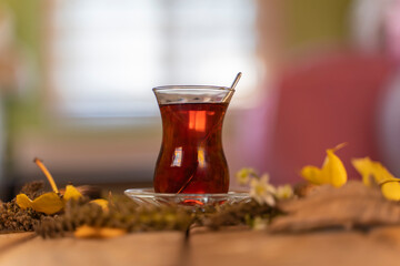 Turkish tea in a glass called thin waist and various natural leaves and plants around it with blurred lights in the background