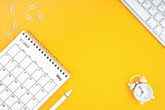May 2025, Monthly desk calendar for 2025 year and alarm clock with paper clips on yellow color background