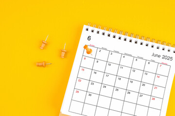 June 2025 Monthly desk calendar for 2025 year with wooden pin on yellow background.