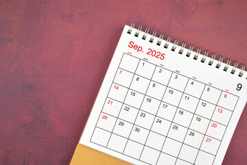 September 2025 desk calendar on red background.