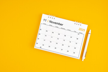 November 2025, Monthly desk calendar for 2025 year and pen on yellow background.
