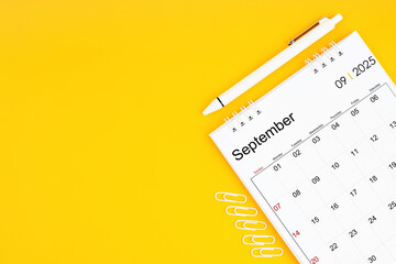 September 2025, Monthly desk calendar for 2025 year and pen with paper clips on yellow color background.