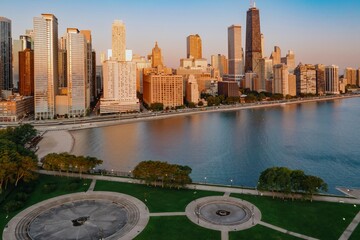 Fototapeta premium Chicago skyline at dawn, reflecting on Lake Michigan. Park and fountain in foreground. Beautiful city view. Milton Lee Olive Park, Chicago, Illinois, United States Of America