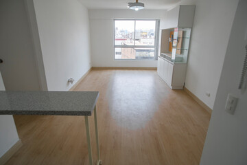Vista de sala de departamento con amplia mampara con vista a la calle , con acabados modernosm, piso de madera y paredes blancas 