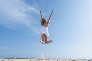 Obraz premium Mujer joven saltando de emoción porque esta feliz y divertida, con un sensacional día de vacaciones en verano en la playa, soleado con cielo azul.