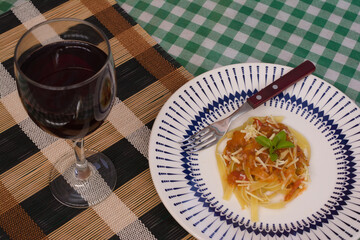 A plate of fettuccine with tomato sauce, cheese, and basil paired with a glass of red wine, set on a checkered tablecloth with earthy tones.