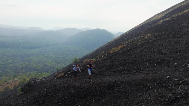 Couple hiking uphill rocky volcano in Mexico. Paricutin Volcano, Michoacan, Mexico during cloudy day. Aerial tracking shot.