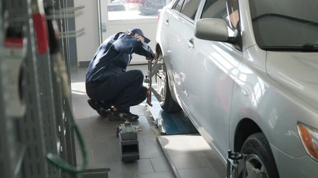 Mechanic performing a wheel alignment process in a modern workshop. Professional equipment is used to ensure accurate vehicle alignment for optimal performance and safety