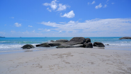 A serene beach view with large, smooth rocks scattered across the soft white sand and a few small...