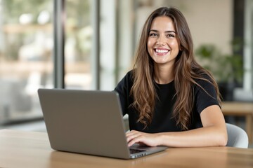Smiling woman sitting at a desk using a laptop in a bright, modern office setting, with natural light and blurred green background, concept of work. Ai generative.