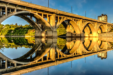 A bridge with a reflection of the sky and the city in the water