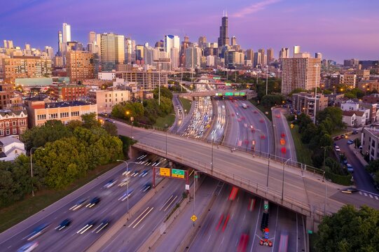 Chicago highway traffic at dusk. Cars blur across the interstate, under a highway overpass, as the sun sets over the city skyline. Interstate 90, Chicago, Illinois, United States