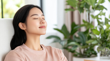 Korean woman in pajama sitting on comfortable sofa with eyes closed and relaxing