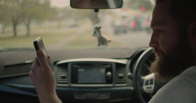 A man is parked on the side of the road as traffic passes by, he is looking outside his passenger window with worry as he talks to someone over the cars internal phone