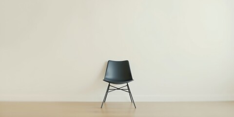 A single dark chair sits against a minimalist off-white wall in a modern, empty room.