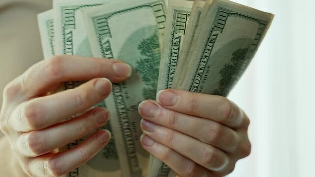 Close-up view of female hands counting a stack of us dollar bills, showcasing the tactile interaction with cash and the significance of money in personal finance and wealth management