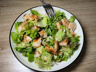 A plate of fresh Caesar salad with grilled chicken, lettuce, and creamy dressing.