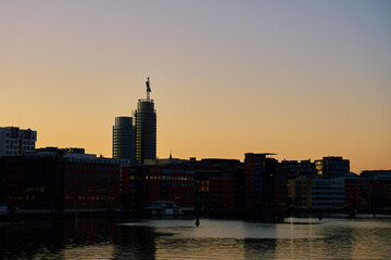 Obraz premium Silhouetted cityscape with modern office buildings along waterfront at sunset. Contemporary architecture. Panoramic view on city embankment