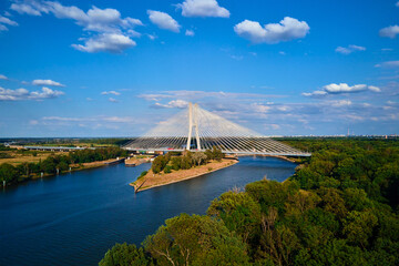 Cable stayed bridge over river surrounded by lush green forest. Redzinski bridge over Odra river with cars driving on highway in Wroclaw, Poland