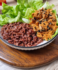 A close-up of a healthy meal with shredded chicken, brown rice, and lettuce leaves on a plate