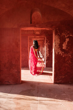 Indian woman wearing saree walking in a red sandstone corridor, Agra, India