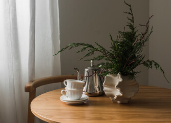 Tea cups, teapot, decorative bouquet on a round wooden table in the living room