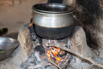 Traditional rural kitchen setup with firewood stove, cooking pot, and utensils in a rustic setting, showcasing old-fashioned cooking methods.