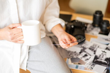 Professional female photographer drinking coffee, reviewing printed images at modern workspace desk
