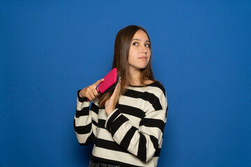 Pretty hispanic teenage girl wearing striped sweater happy brushing her silky hair with a brush,...
