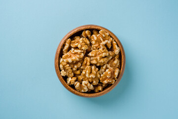 Top view of heap of walnut kernels in wooden bowl on blue background