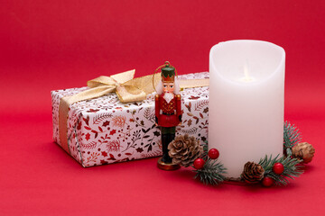 Christmas concept, red background, nutcracker and candle next to wrapped gift box on red background 
