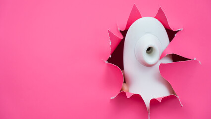 White vacuum clitoral vibrator sticking out through pink paper background. Sex toy. 